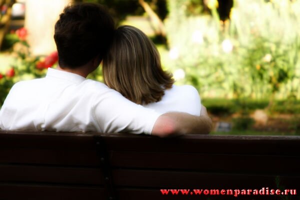 Влюбленная пара сидит обнявшись на скамейке